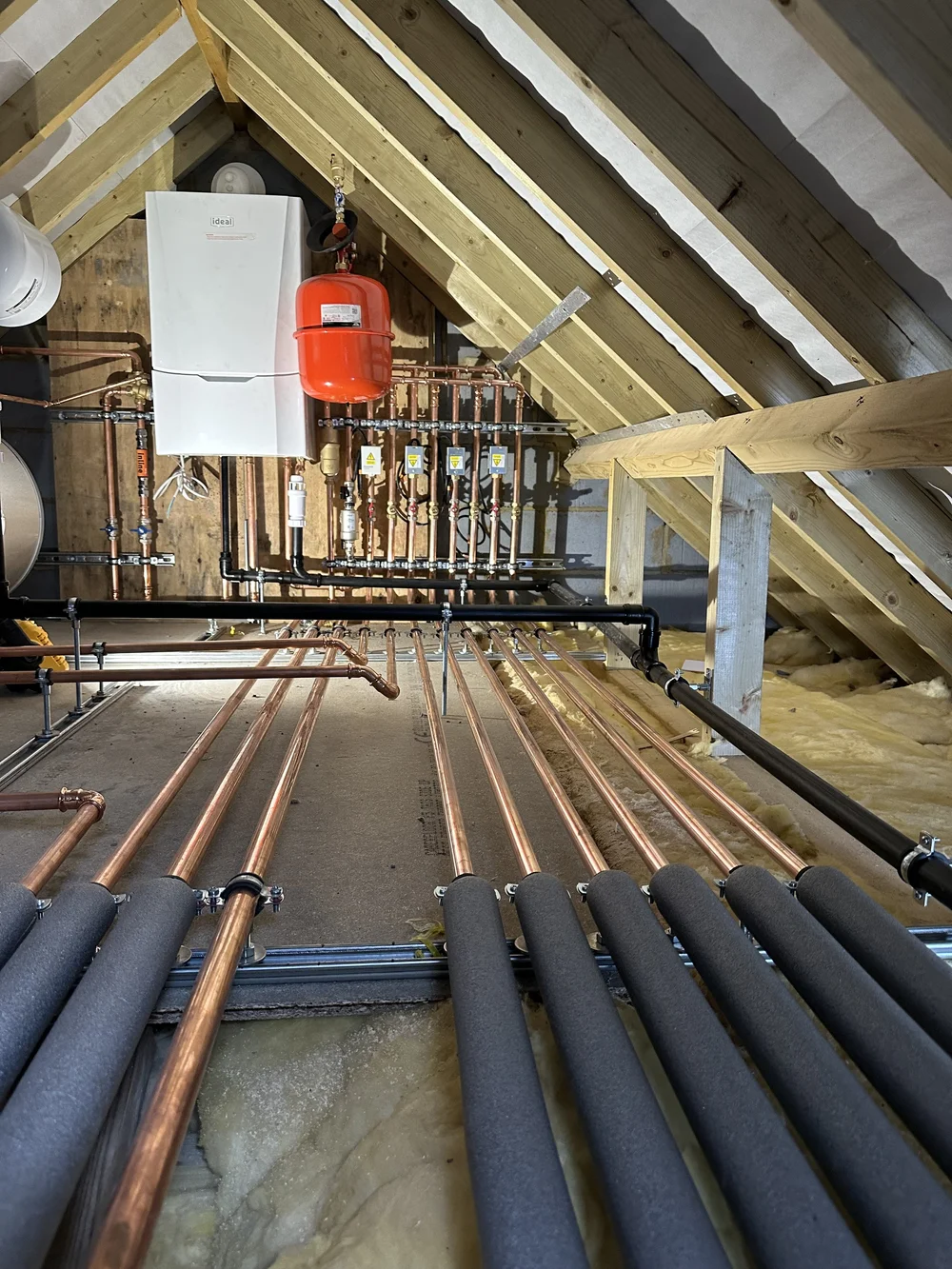 Loft boiler installation with insulated copper pipework across floor joists — plumbing Haslemere