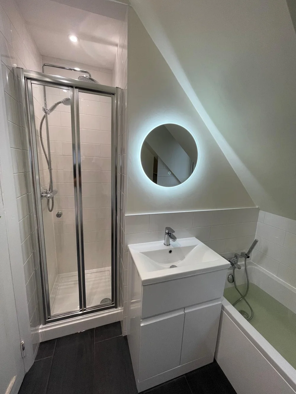 Compact loft shower room with backlit round mirror and bi-fold shower door — bathroom renovation Haslemere