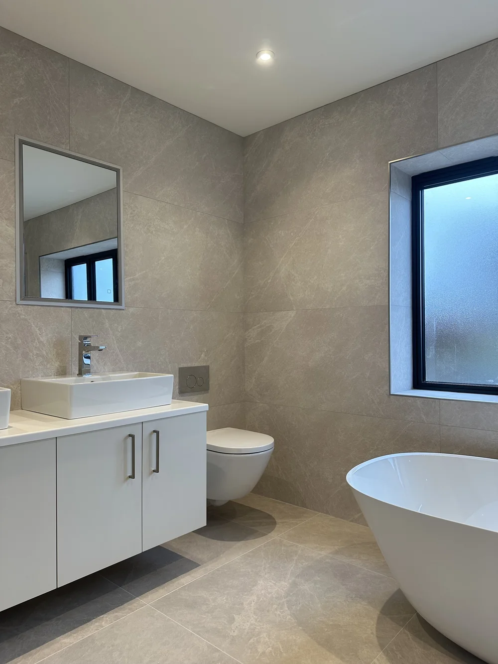Contemporary stone-tiled bathroom with freestanding bath, floating vanity and twin basins — bathroom renovation Haslemere