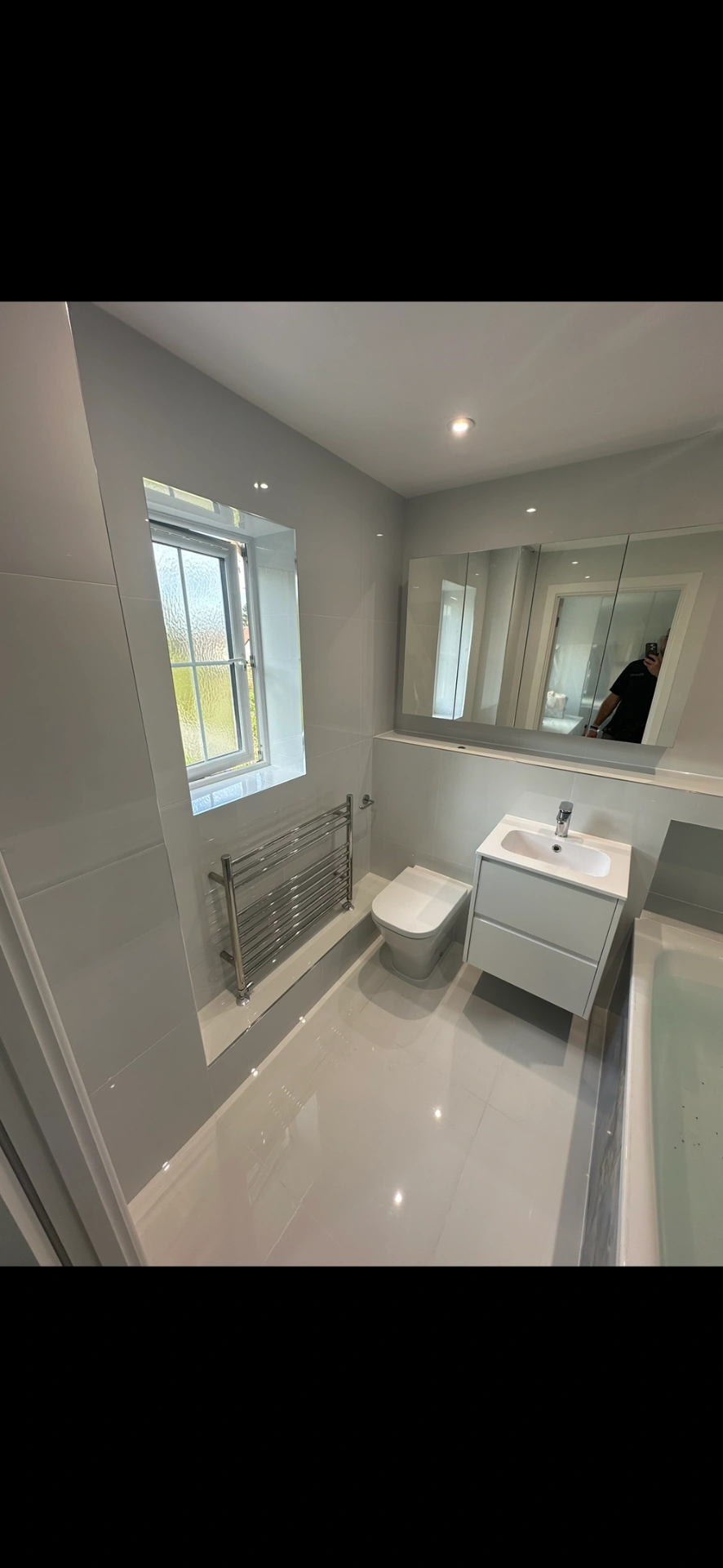 Bright white family bathroom with floating vanity, mirrored cabinet and gloss floor tiles — bathroom installation Haslemere