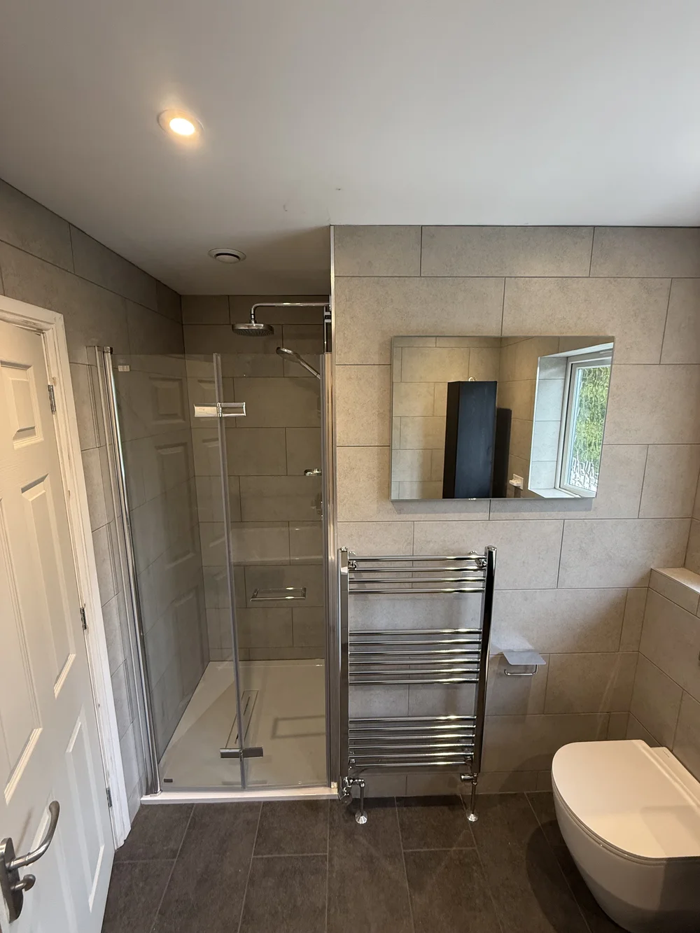 Stone-tiled family bathroom with hinged glass shower enclosure and chrome towel rail — bathroom installation Haslemere