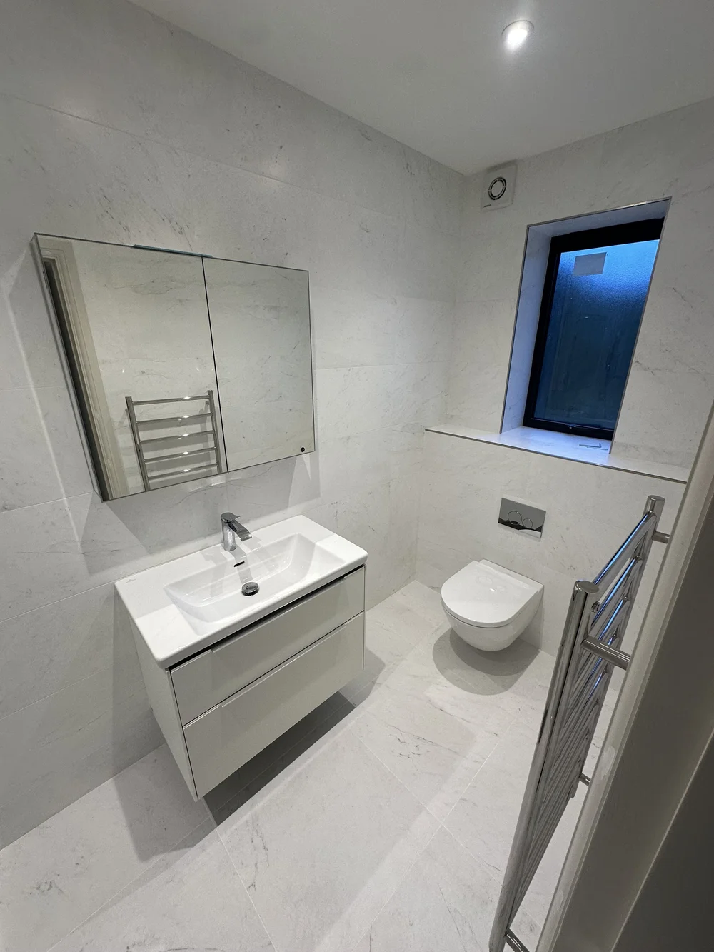 White marble ensuite with wall-hung vanity, mirrored cabinet and back-to-wall WC — Haslemere