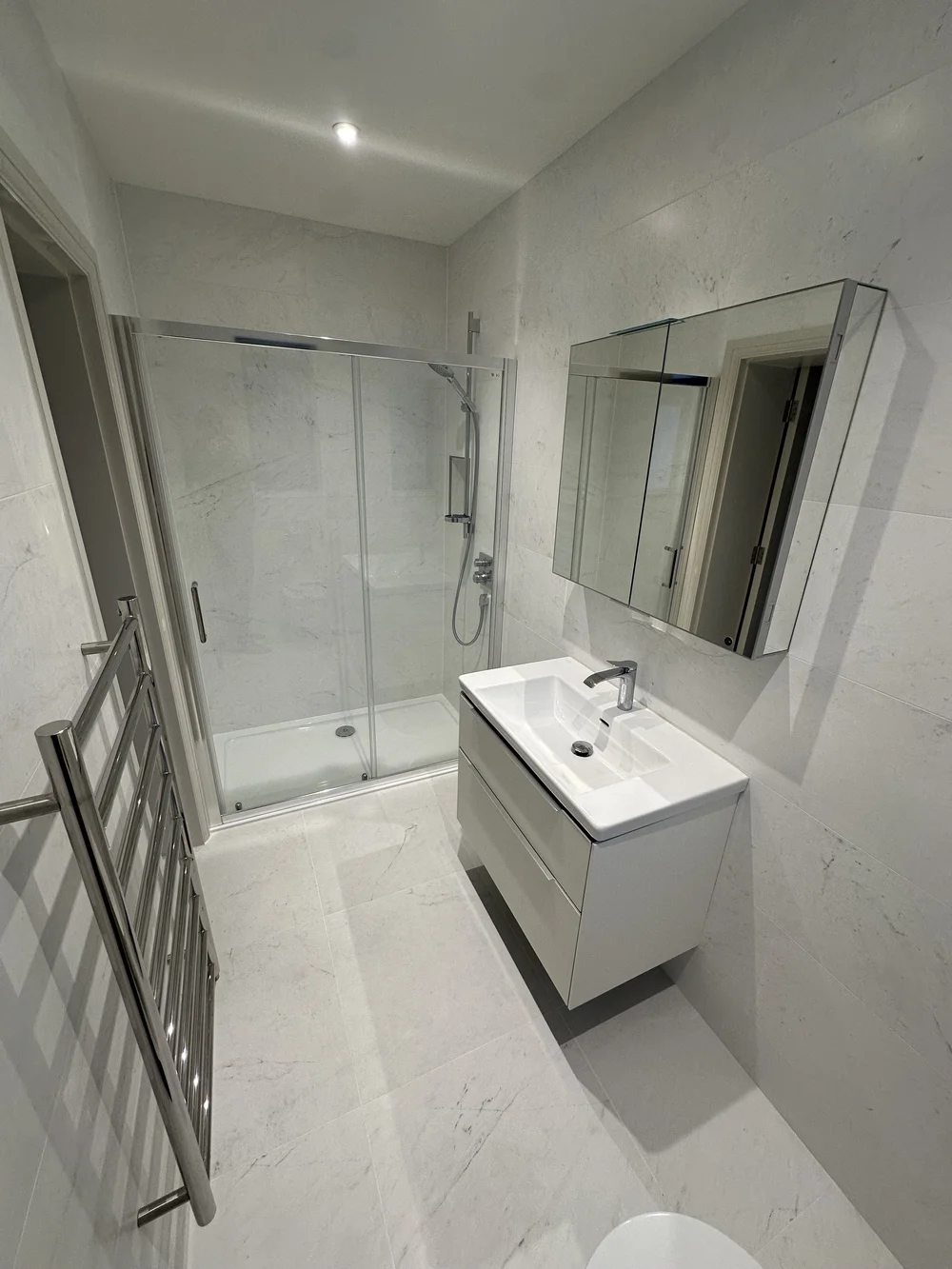 White marble shower room with sliding enclosure, wall-hung vanity and heated ladder rail — bathroom installation Haslemere