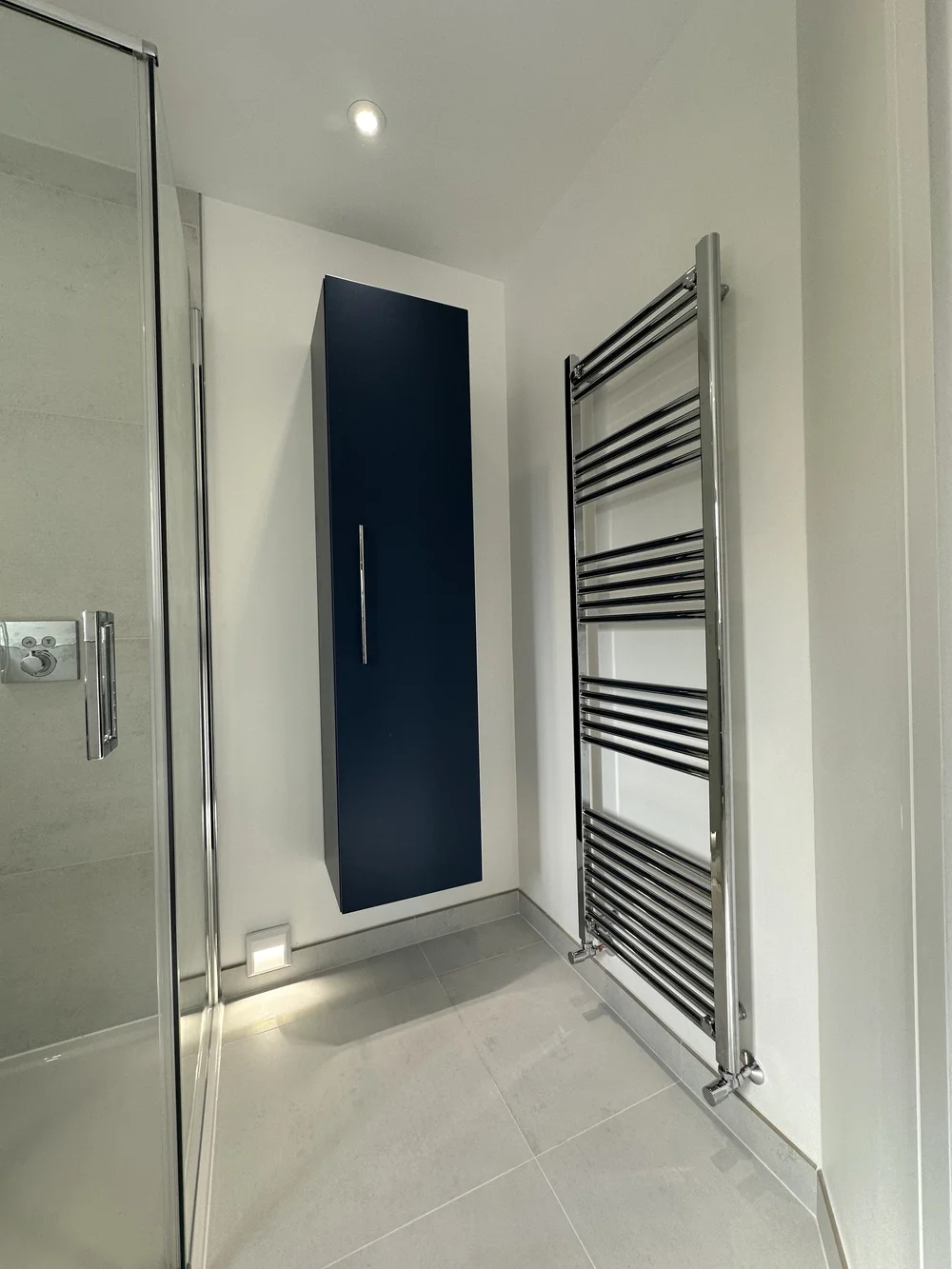 Detail of navy wall-hung storage cabinet with chrome ladder radiator — bathroom design Haslemere