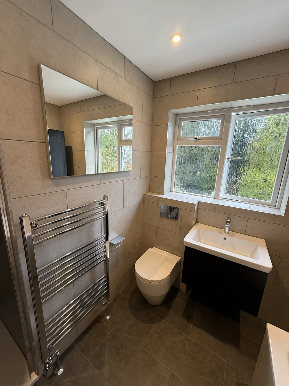Beige-tiled bathroom with wall-hung black vanity and chrome heated rail — bathroom renovation Haslemere