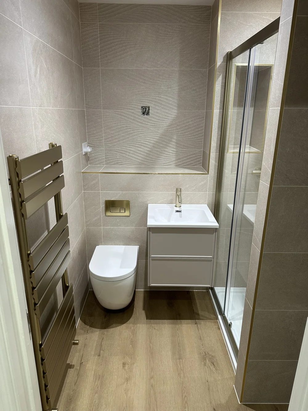 Textured stone shower room with brushed brass trim and designer towel rail — bathroom installation Haslemere