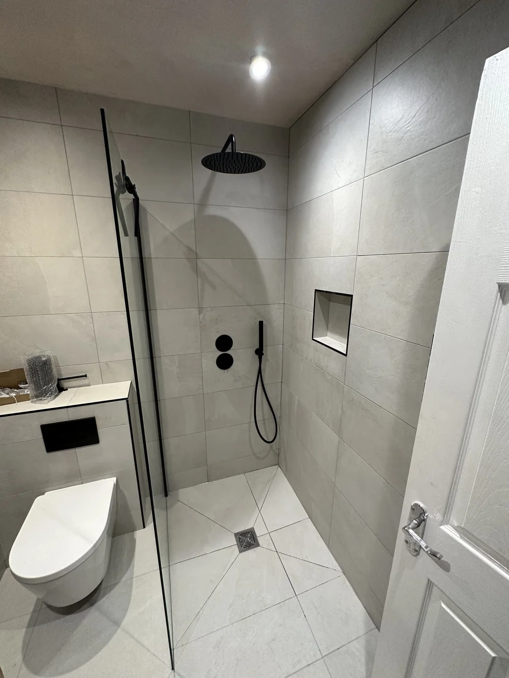 Stone-tiled walk-in shower with matte black rainfall head and recessed niche — wet room Haslemere
