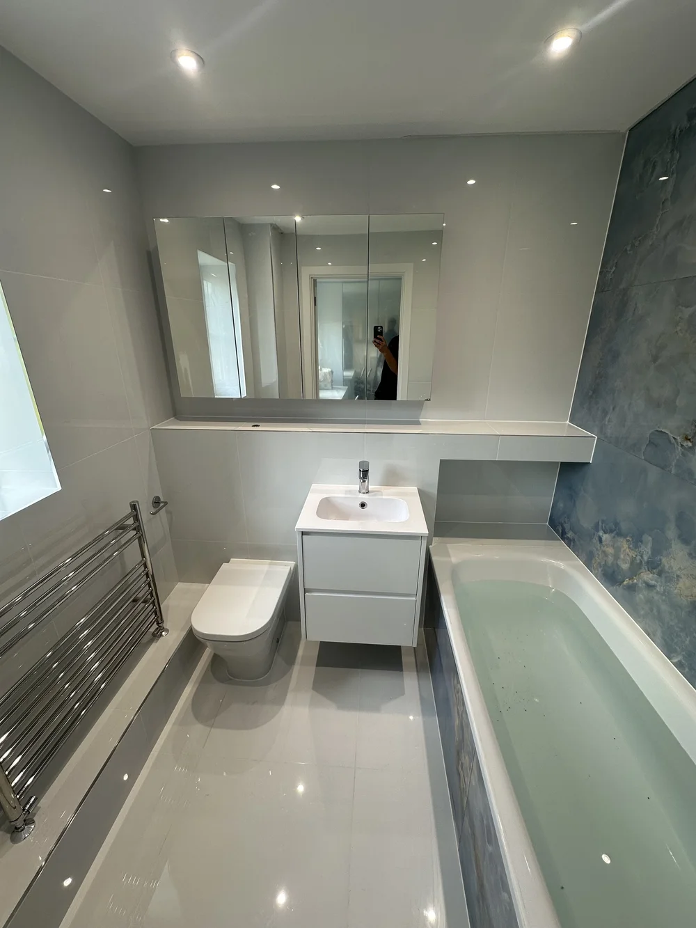 Bright family bathroom with mirrored cabinet, white vanity and blue onyx accent wall — bathroom renovation Haslemere