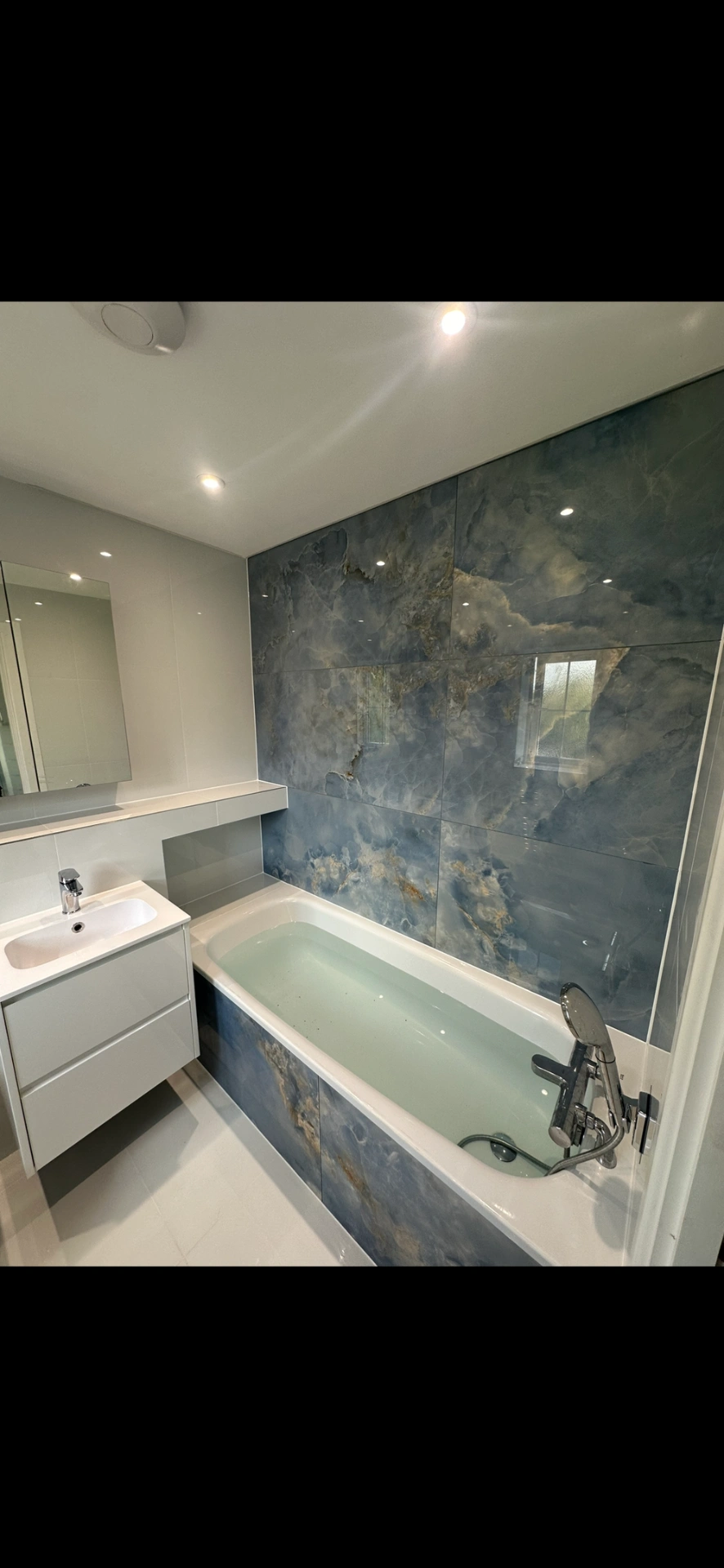 Bathroom with blue onyx-effect feature wall, panelled bath and floating white vanity — bathroom renovation Haslemere