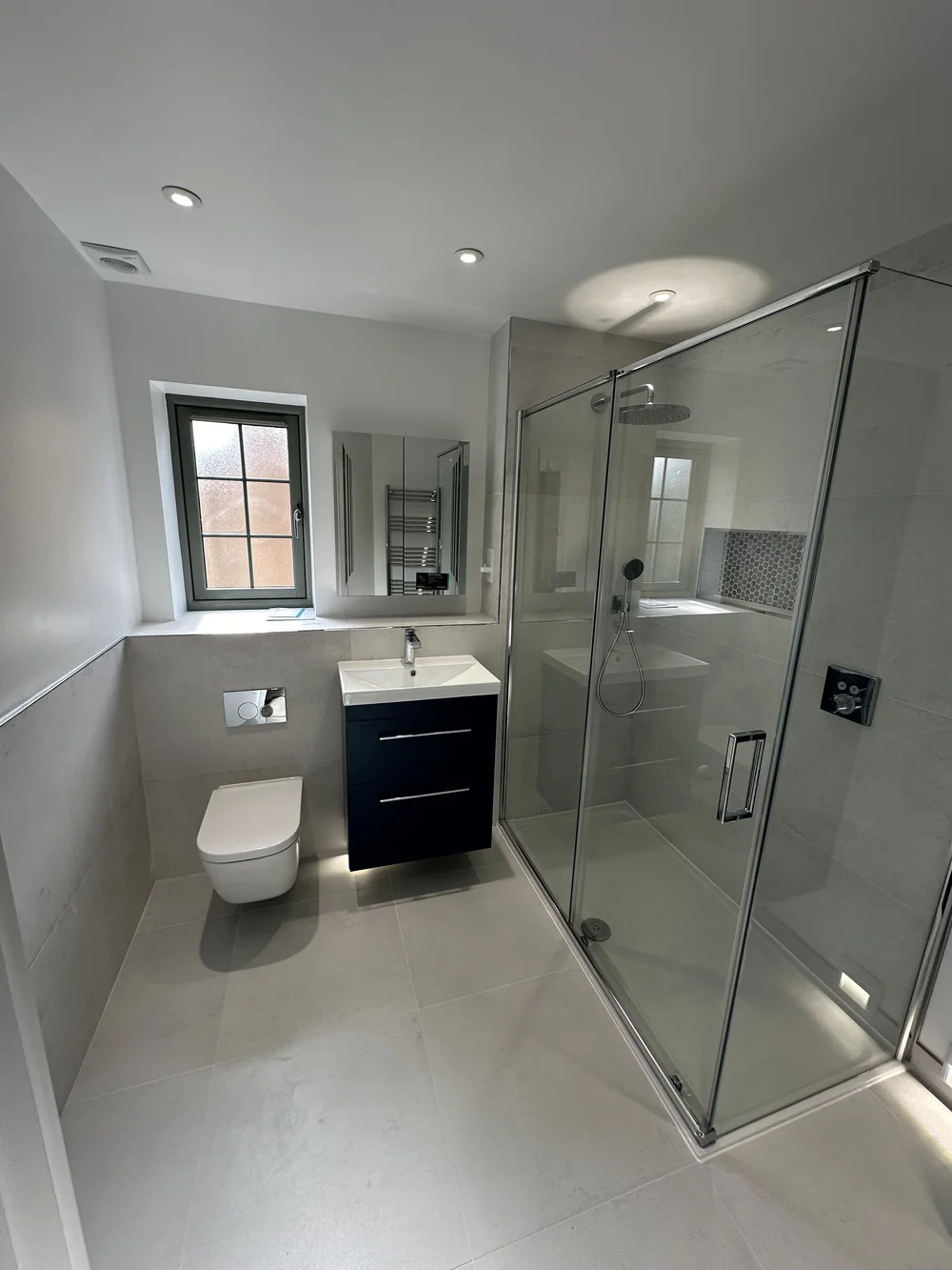 Fitted shower room with navy vanity, wall-hung WC and large glass shower enclosure — bathroom installation Haslemere