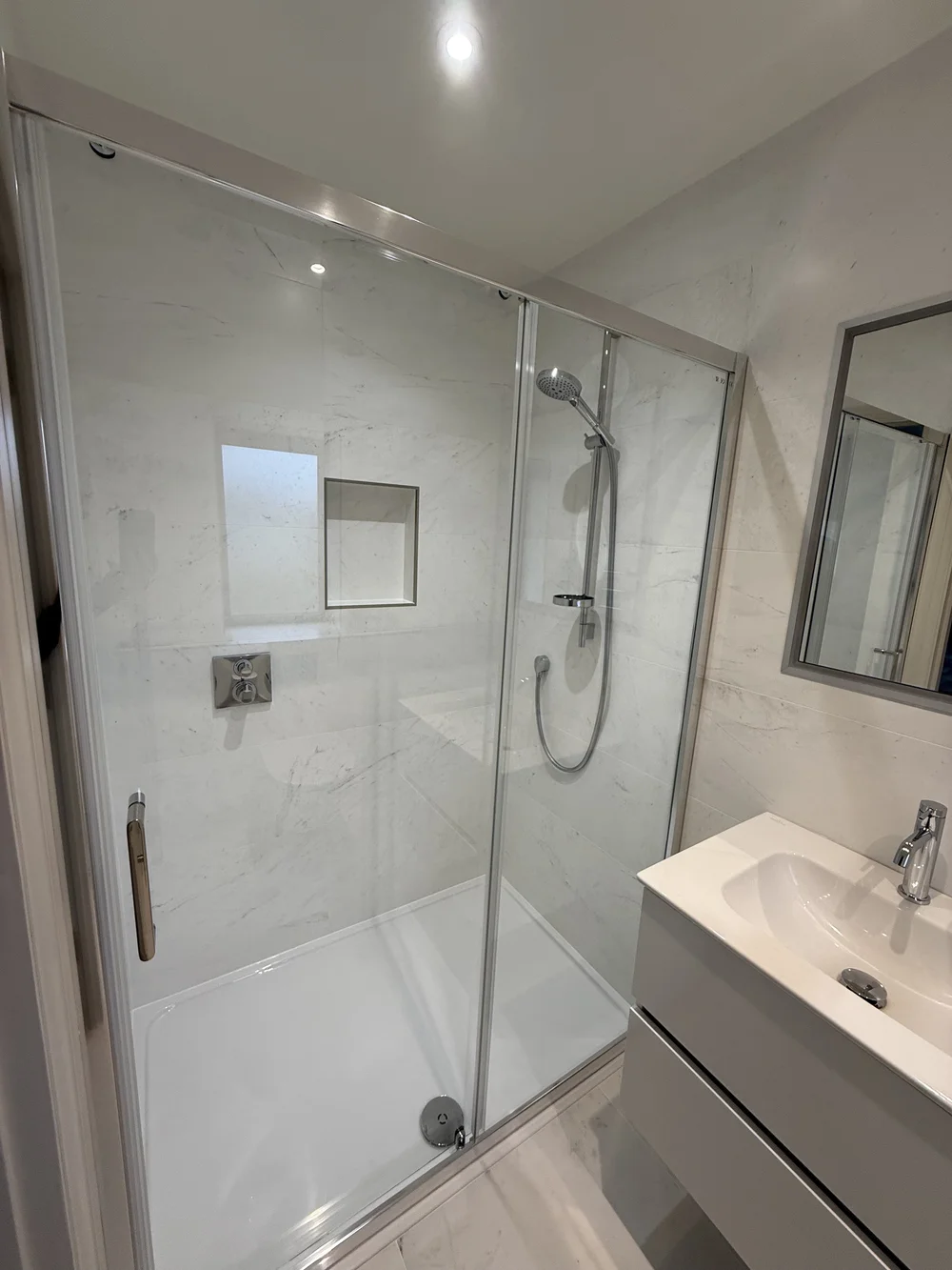 Marble shower enclosure with sliding door and recessed niche — bathroom renovation Haslemere