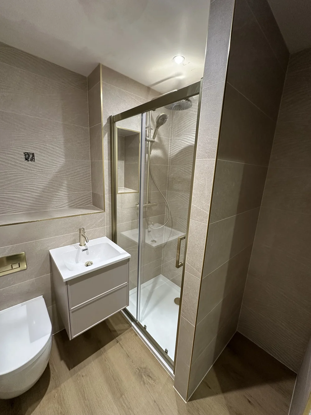 Wave-tiled shower room with brushed brass fittings and oak-effect floor — bathroom renovation Haslemere
