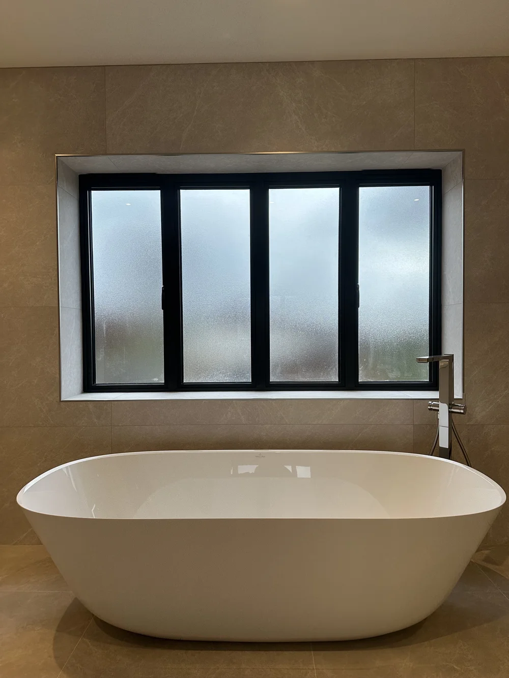 Freestanding stone-resin bath under crittall window in marble master bathroom — bathroom installation Haslemere